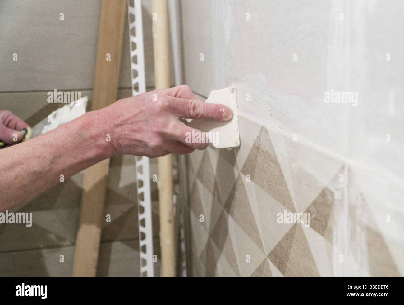 Lavoratore con una spatola in gomma riempire le giunzioni con una soluzione. Lavori di finitura, messa a fuoco sfocata. La tecnologia di posa delle piastrelle Foto Stock