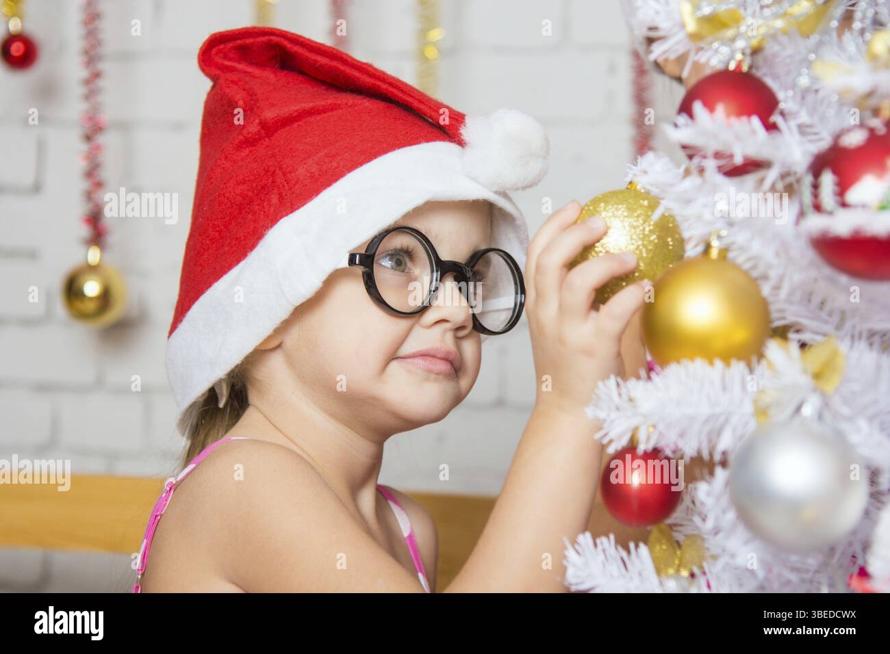 Ragazza con bicchieri arrotondati si blocca le sfere su un nuovo nevoso anni albero di Natale Foto Stock
