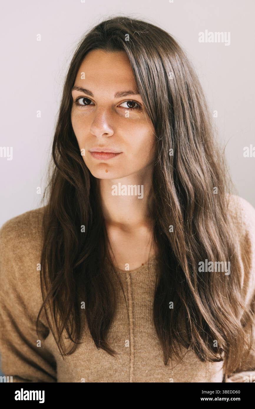 La giovane e millenaria bella donna a casa seduta sul divano. Ritratto sicuro e sano. Lunghi capelli castani e grandi occhi bella donna. Foto Stock