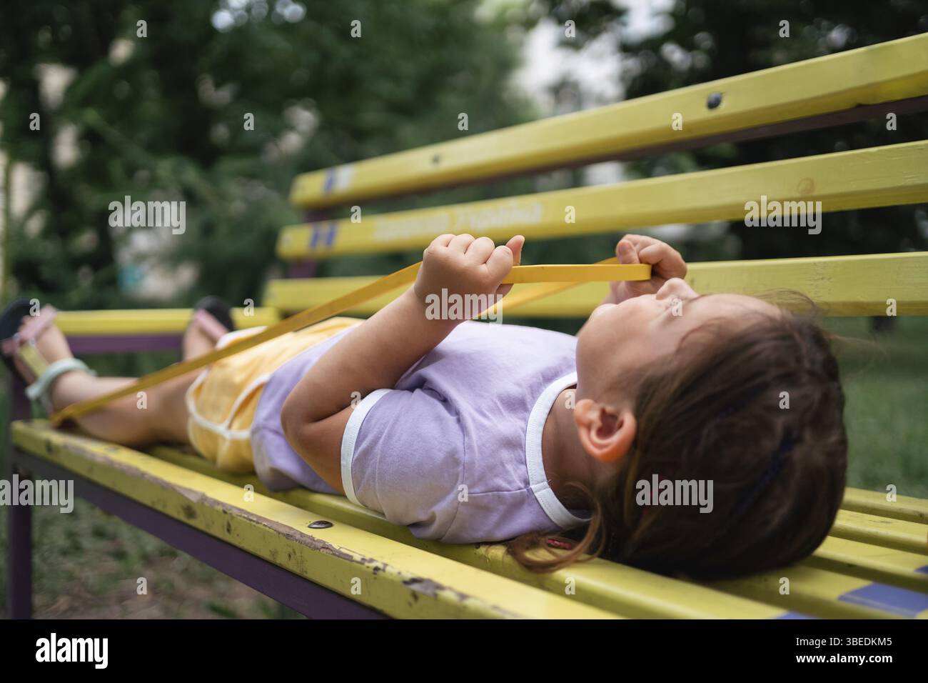 Bambina che fa esercizi di allenamento con fasce di resistenza sulla panchina nel parco. Foto Stock