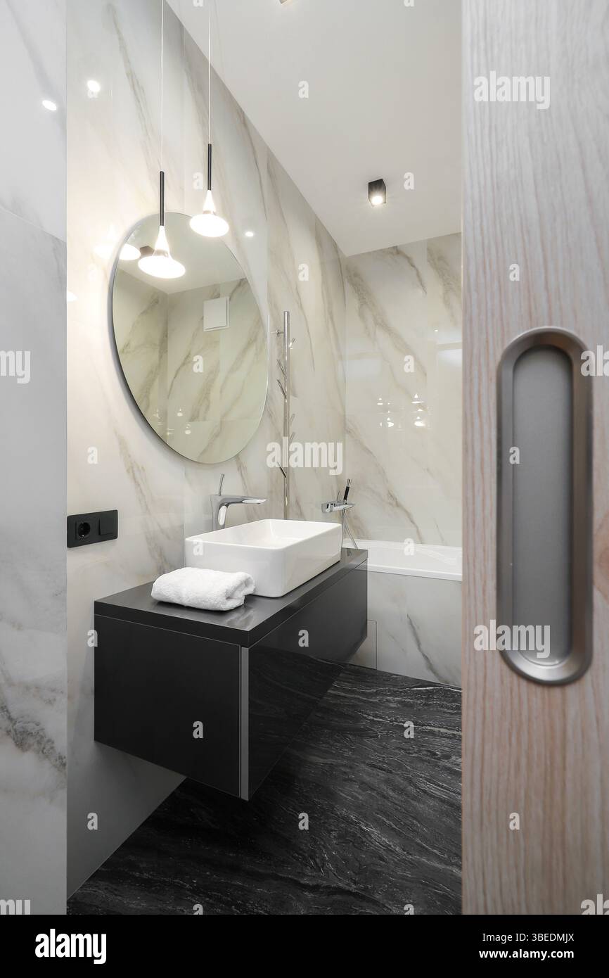 Rubinetto con lavandino in ceramica e specchio rotondo all'interno del bagno Foto Stock Rubinetto con lavandino in ceramica e specchio rotondo all'interno del bagno Foto Stock