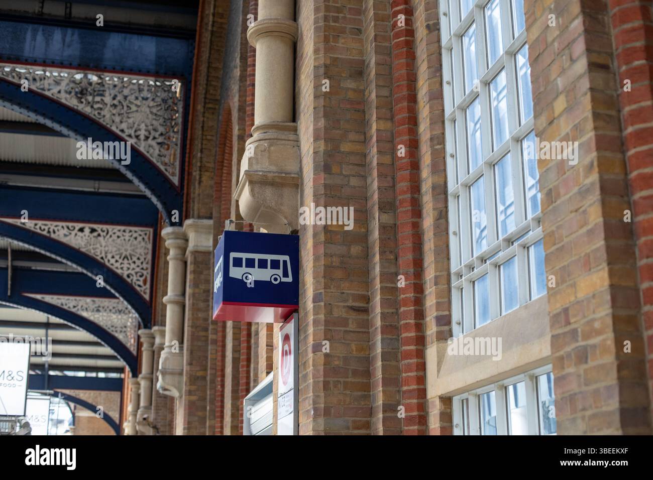 Una vista dettagliata della facciata di un edificio in mattoni con un cartello blu dell'autobus a Londra. L'architettura presenta lavorazioni ornamentali in metallo e grandi finestre. Foto Stock