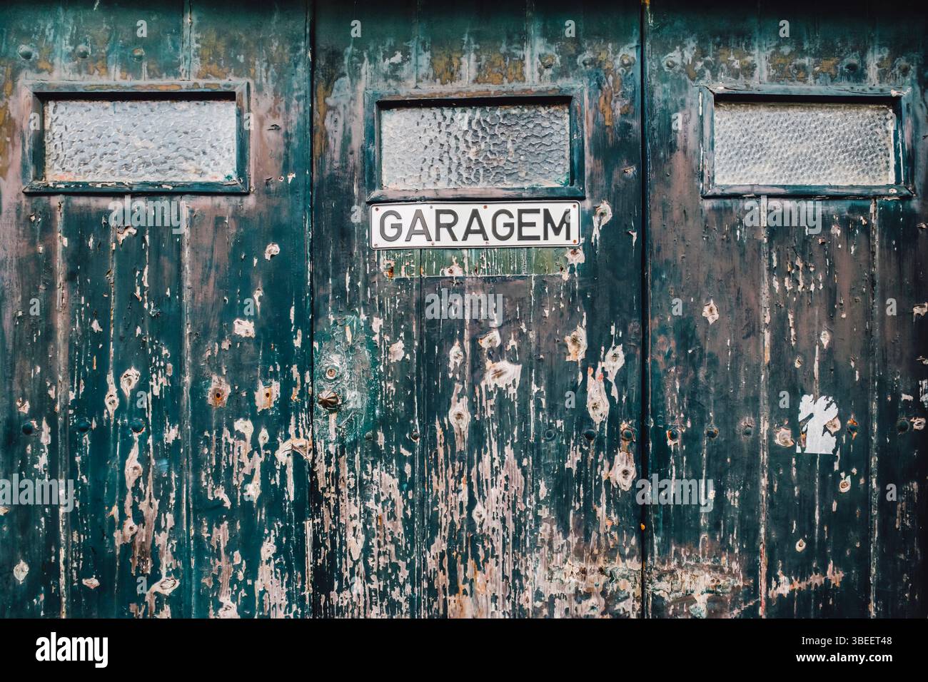 Vecchia porta del garage intemprata con vernice verde e cartello Garagem. Ingresso al garage portoghese vintage, superficie in legno angosciato, architettura rustica, Foto Stock