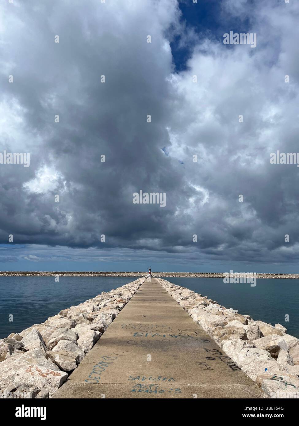 Cielo tempestoso sopra un molo di cemento che si estende nel Mare Adriatico a Bar, Montenegro. Immortalato in una nuvolosa giornata primaverile. - Immagine stock catturata con smartphone