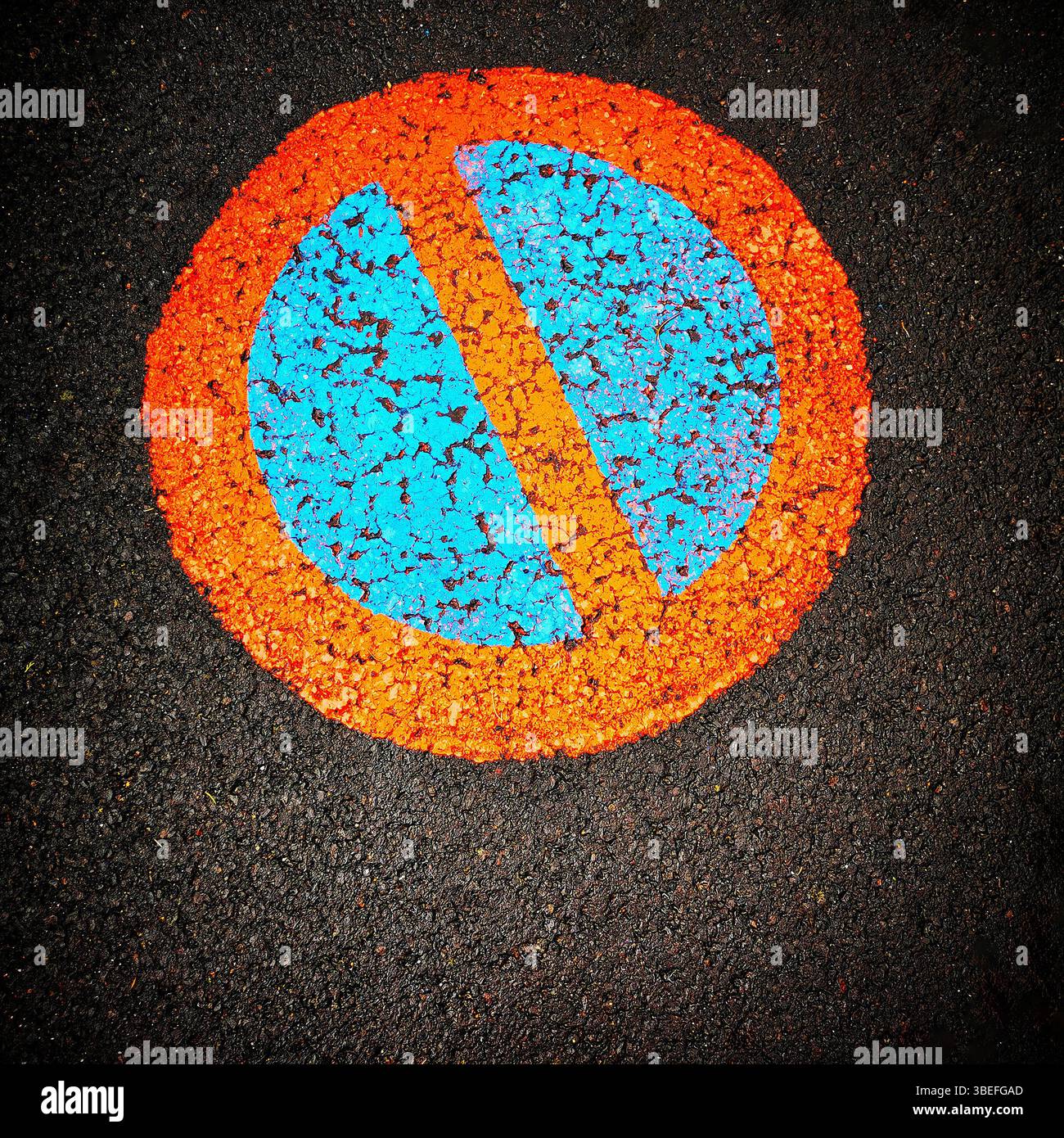 Un simbolo vibrante di divieto di parcheggio viene visualizzato in modo prominente su una superficie di asfalto nera, con un cerchio blu intersecato da una linea diagonale arancione Foto Stock