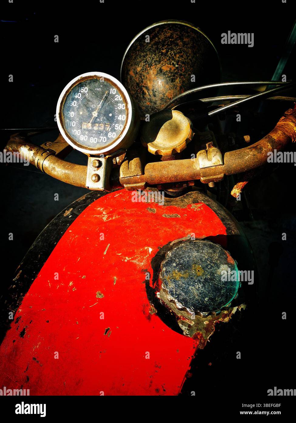 Il cruscotto di una motocicletta usurata presenta un tachimetro arrugginito e un lavoro di verniciatura sbiadito. Lo sfondo scuro enfatizza i componenti obsoleti Foto Stock