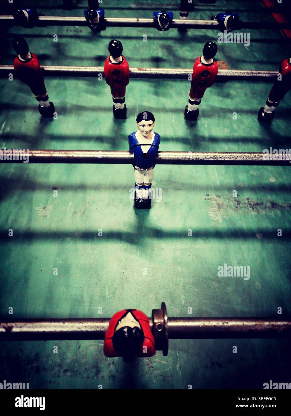 Una vivace partita di calcio a tavolo presenta personaggi diversi in rosso, blu e nero, posizionati su una superficie di gioco verde. Foto Stock