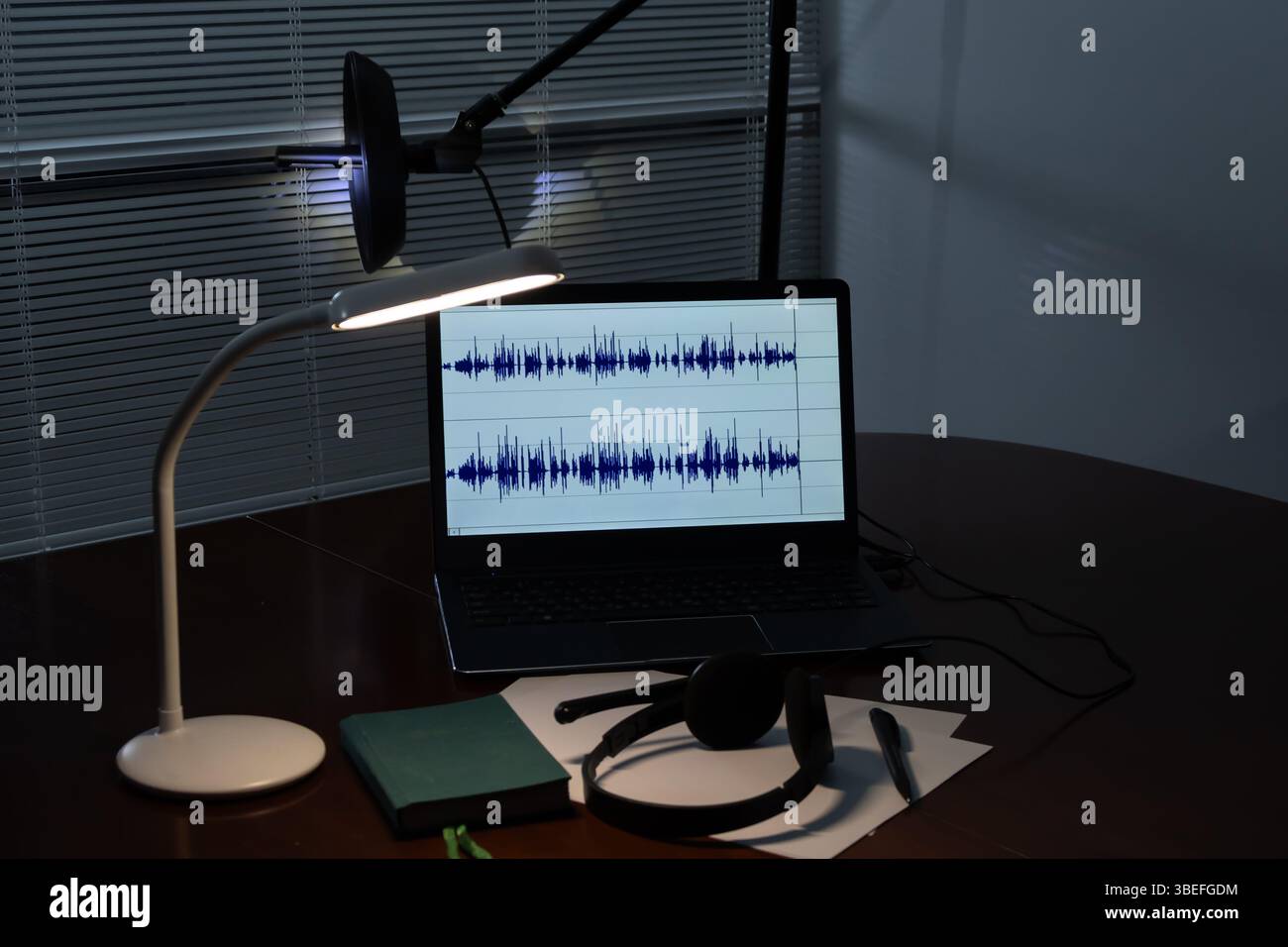 Configurazione dell'ascolto e della registrazione audio: Un computer portatile con display a onde audio, microfono direzionale, cuffie e materiale di scrittura sul tavolo. La truffa Foto Stock