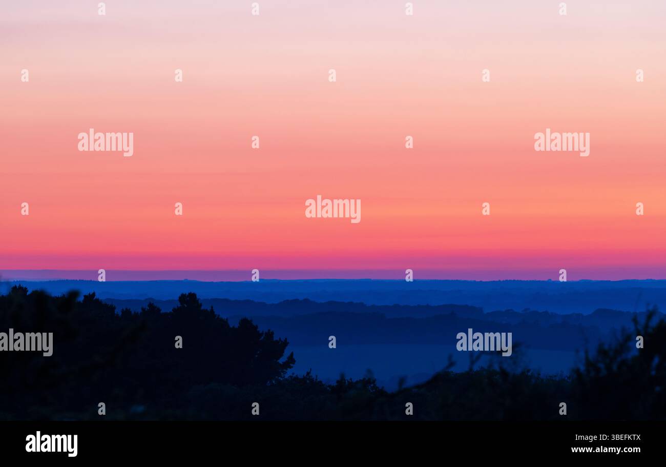 Crepuscolo sull'Isola di Wight, con strati di foresta blu profondi e un vivace cielo magenta-arancione durante una serata estiva nel sud dell'Inghilterra. Foto Stock