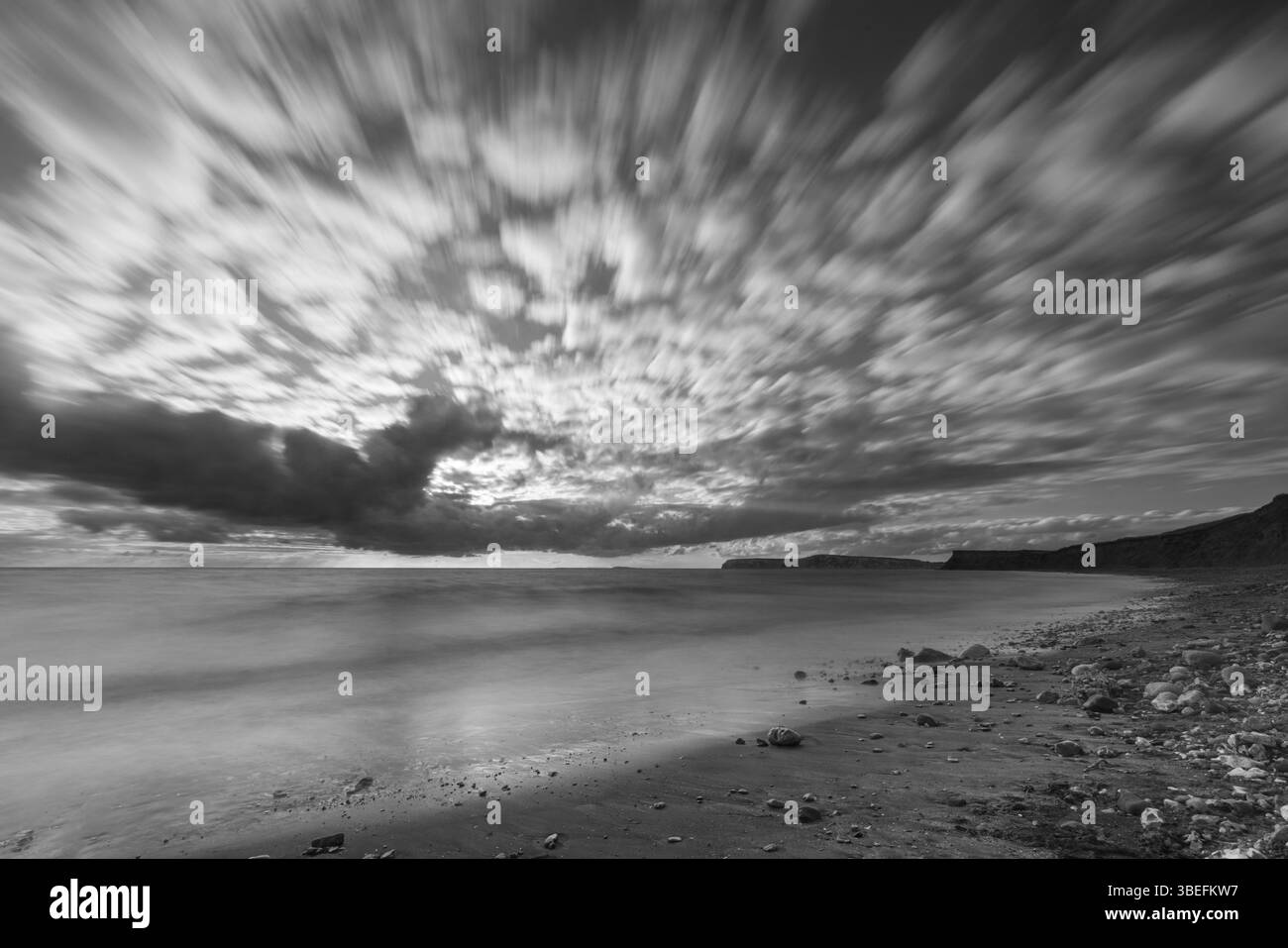 Immagine in bianco e nero a lunga esposizione di spettacolari cieli costieri sull'Isola di Wight, che mostrano striature nuvolose e una costa tranquilla. Foto Stock