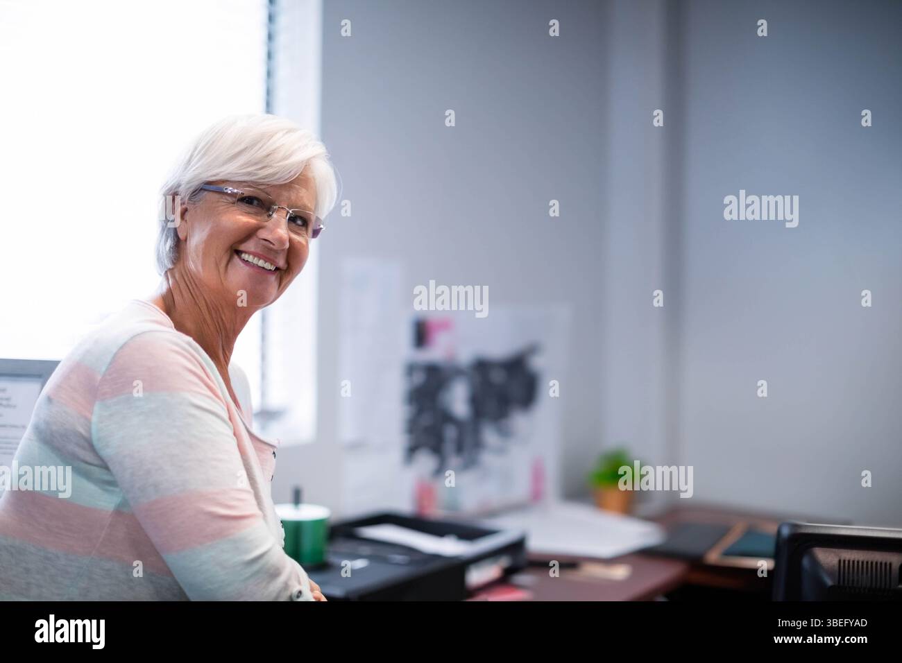 Scrivania da ufficio che tiene la stampante, vassoio con documenti, pianta incapsulata da tende a finestra che lasciano scorrere la luce Foto Stock