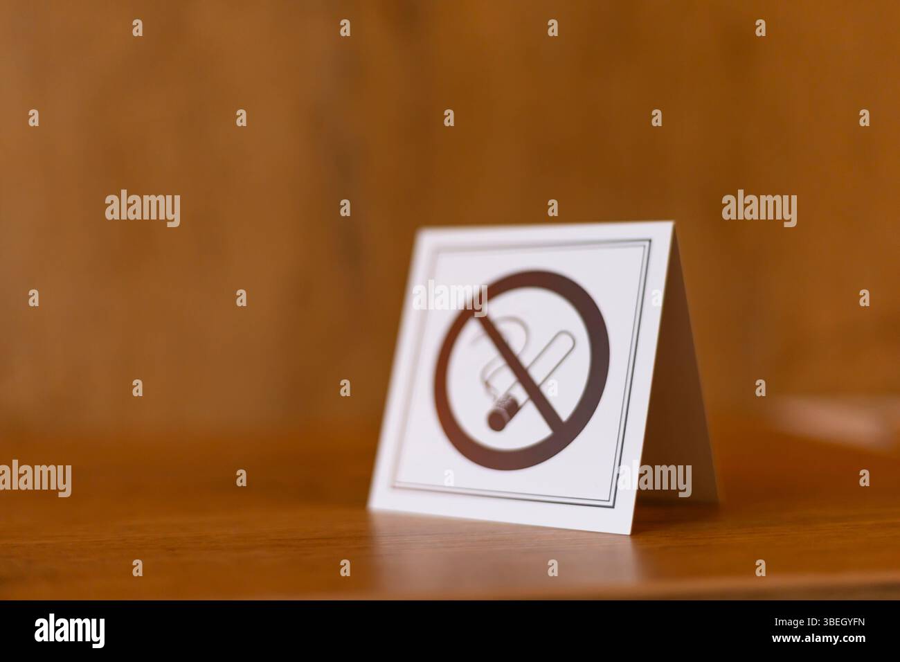 Un cartello con il simbolo del divieto di fumo si erge su un tavolo di legno in un ambiente interno. Il messaggio chiaro mira a promuovere un ambiente senza fumo, migliorando Foto Stock