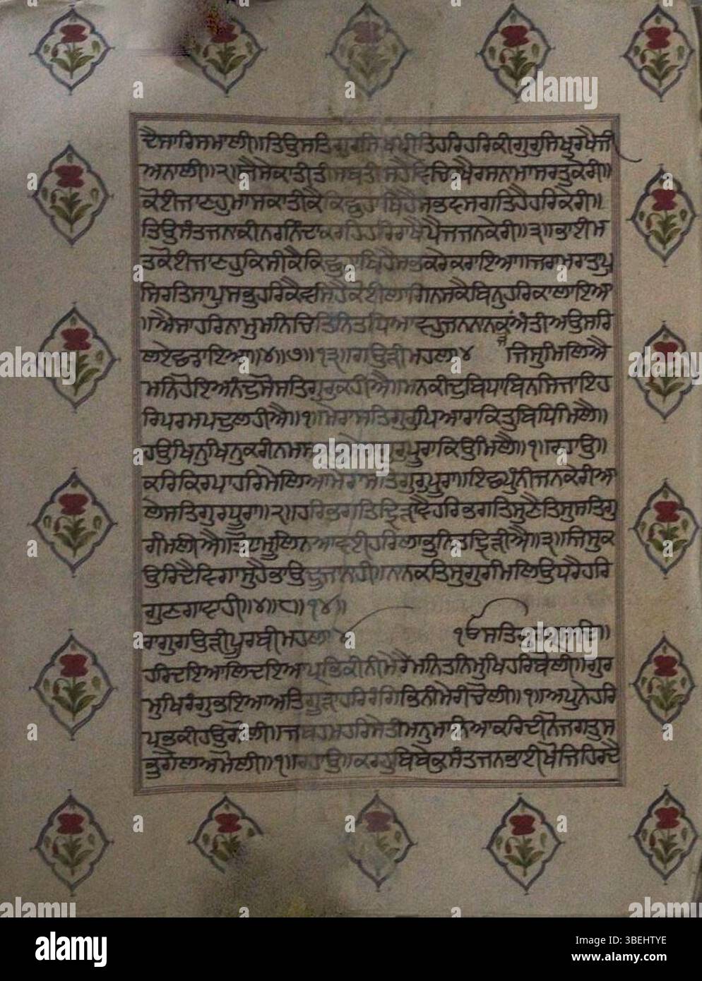 Un folio del manoscritto Guru Granth Sahib, scritto a mano da uno scriba sconosciuto e conservato nella collezione Gurdwara Nanak Shahi a Nilkhet, Dhaka, Bangladesh. Questo manoscritto presenta motivi floreali lungo i confini, che riflettono la tradizione della calligrafia sikh. Si ritiene che il testo, scritto in scrittura Gurmukhi, risalga alla fine del XVI o all'inizio del XVII secolo. Foto Stock