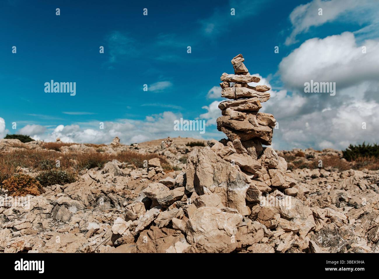 Una pila di roccia accuratamente impilata segna il percorso in montagna, guidando gli escursionisti sotto un cielo blu misto in una giornata soleggiata e limpida Foto Stock