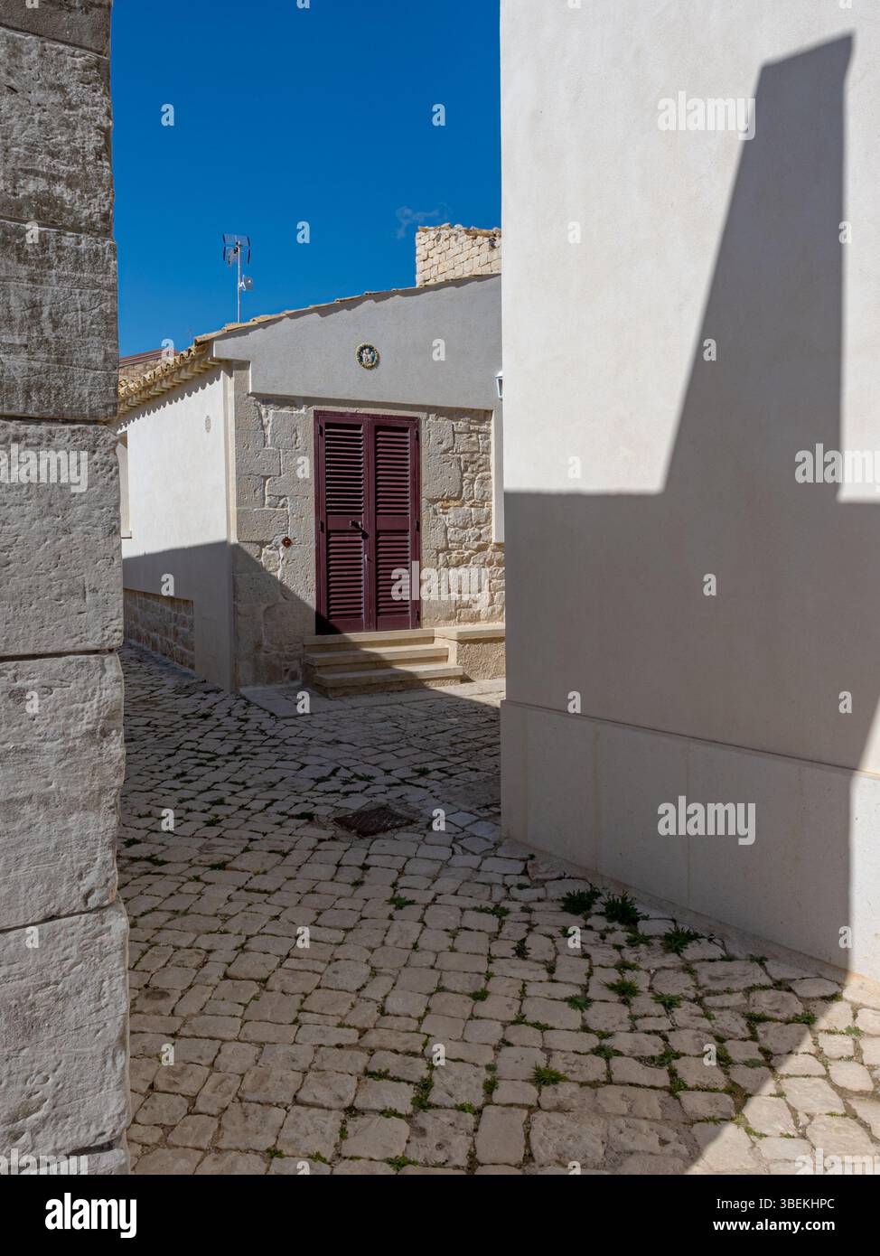Strada stretta di un villaggio siciliano con una sola porta, presa in una soleggiata giornata invernale senza gente. Foto Stock