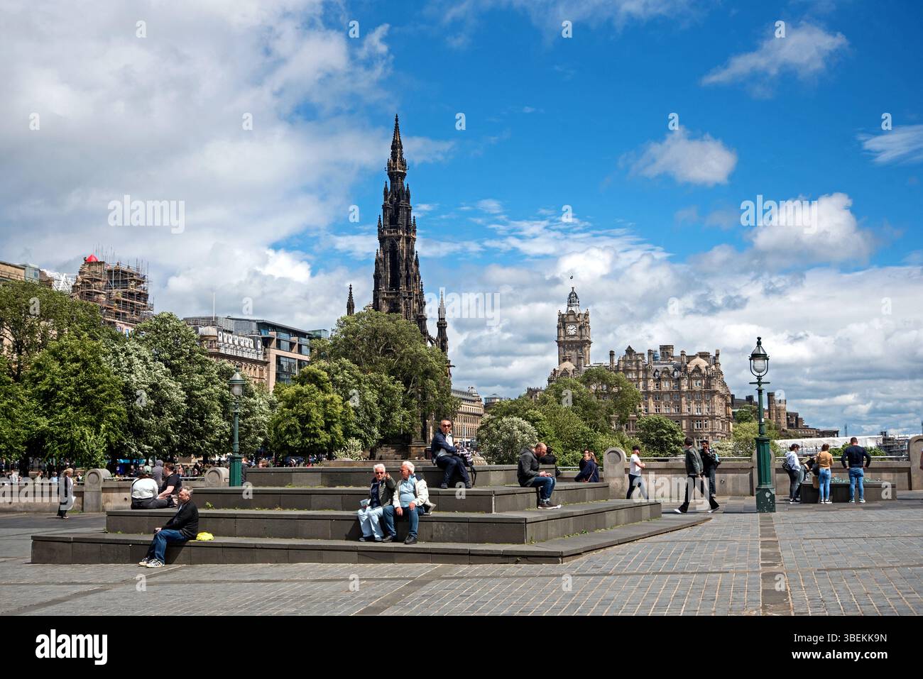Persone che si godono il sole primaverile al Mound con lo Scott Monument e il Balmoral Hotel sullo sfondo a Edimburgo, Scozia, Regno Unito. Foto Stock