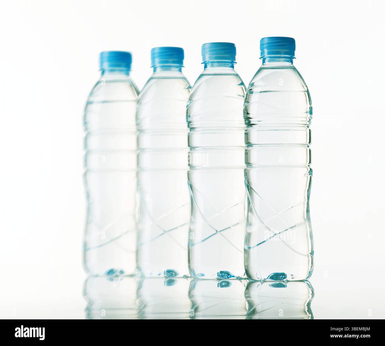 Quattro bottiglie d'acqua in plastica trasparente con tappi blu si stagliano in linea retta e creano riflessi morbidi sulla superficie lucida sottostante. Lo sfondo è un cl Foto Stock