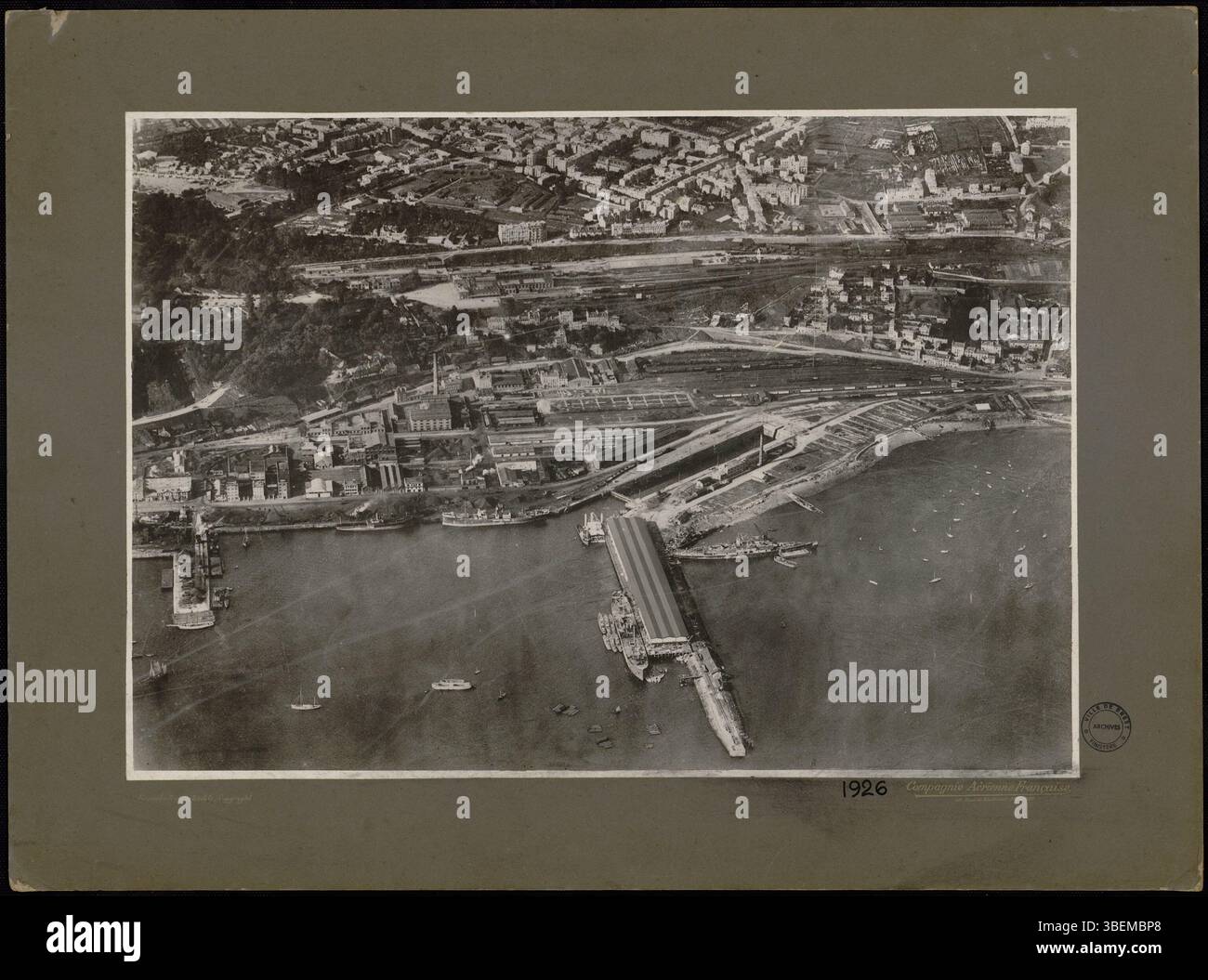 Questa fotografia aerea di Brest, scattata dalla compagnie Aérienne francese nel 1926, presenta una vista obliqua dal porto. In primo piano, l’area portuale è visibile, con la stazione ferroviaria sullo sfondo, offrendo un’istantanea delle infrastrutture della città durante quel periodo. Foto Stock