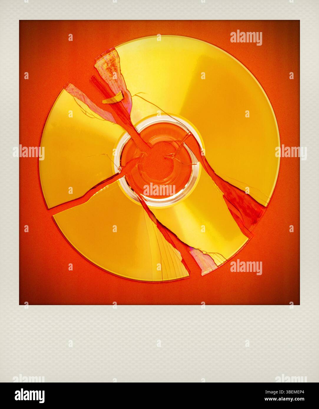 Un CD polaroide rotto si trova su una superficie rossa brillante, mostrando più incrinature irradiate dal centro, evidenziandone lo stato di danneggiamento. Foto Stock