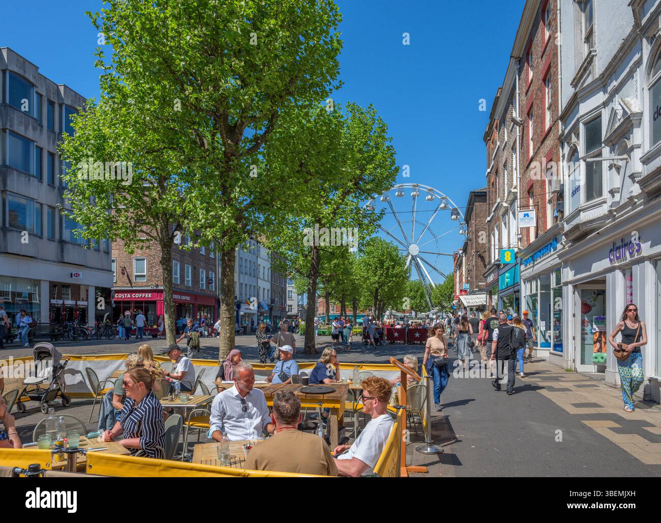 Caffè e negozi in Parliament Street con la ruota di York sullo sfondo, York, North Yorkshire, Inghilterra, Regno Unito Foto Stock