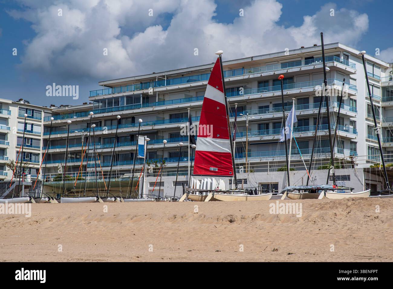 Un catamarano su una spiaggia sabbiosa in Bretagna, nella città di la Baule, con la sua vela rossa e bianca di fronte ad appartamenti Foto Stock