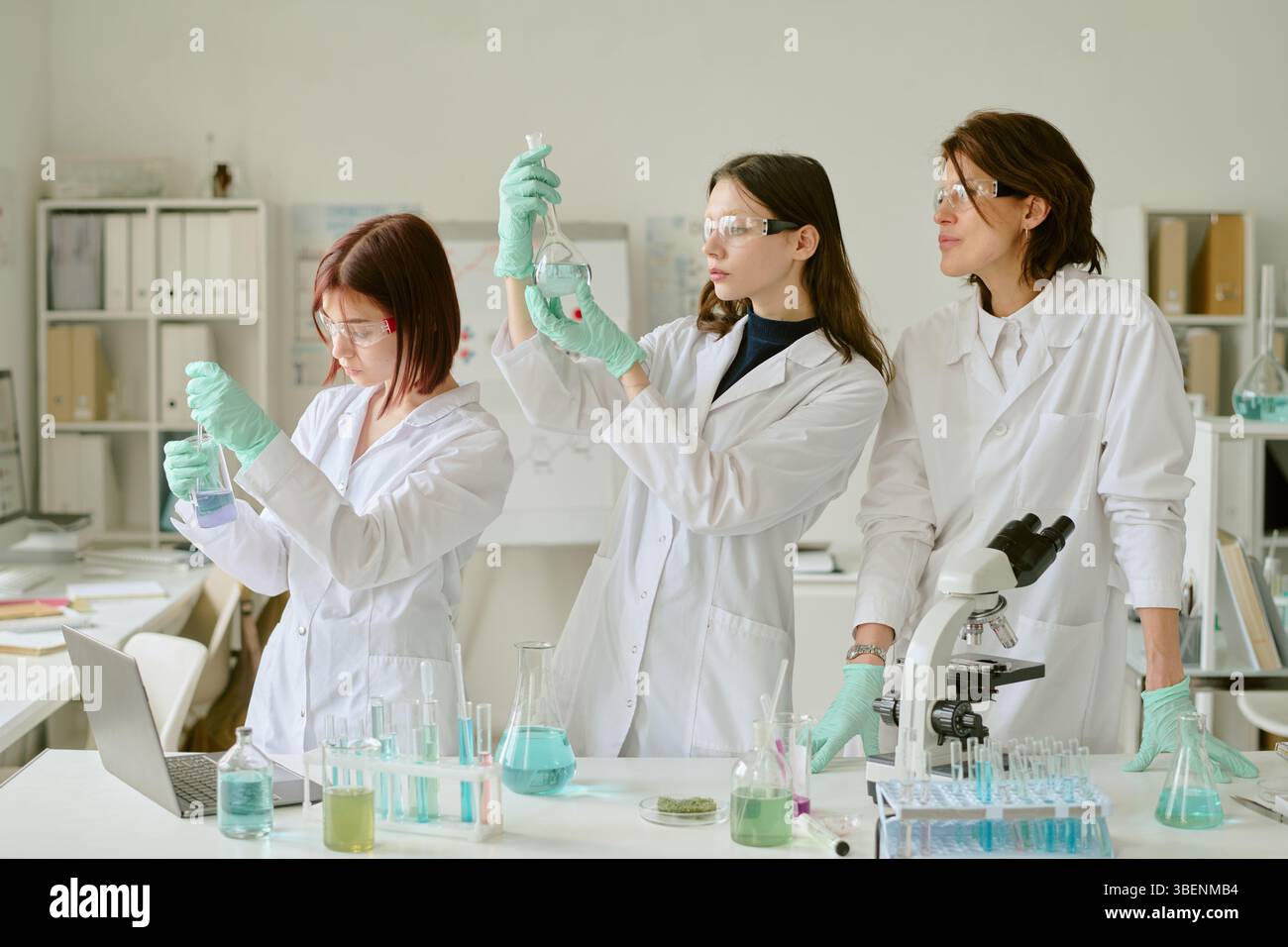 Tre scienziati di laboratorio analizzano campioni mentre lavorano al processo di verifica degli esperimenti con vari strumenti e dispositivi scientifici in una r ben illuminata Foto Stock