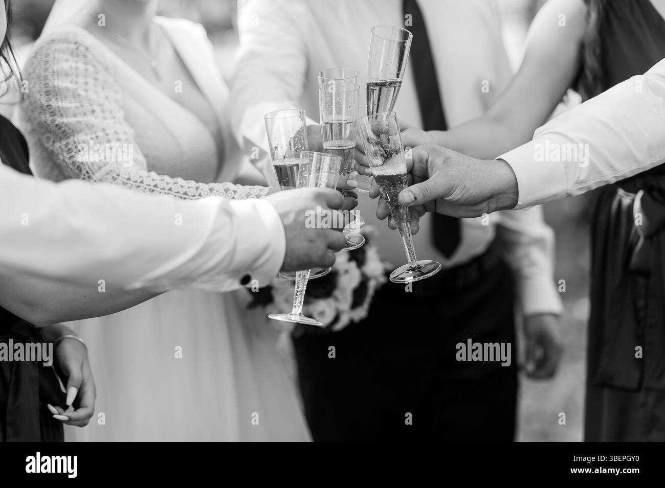 Una gioiosa scena di celebrazione del matrimonio in bianco e nero con diverse persone che alzano bicchieri da champagne in un brindisi tra la sposa in abito in pizzo è visibile Foto Stock