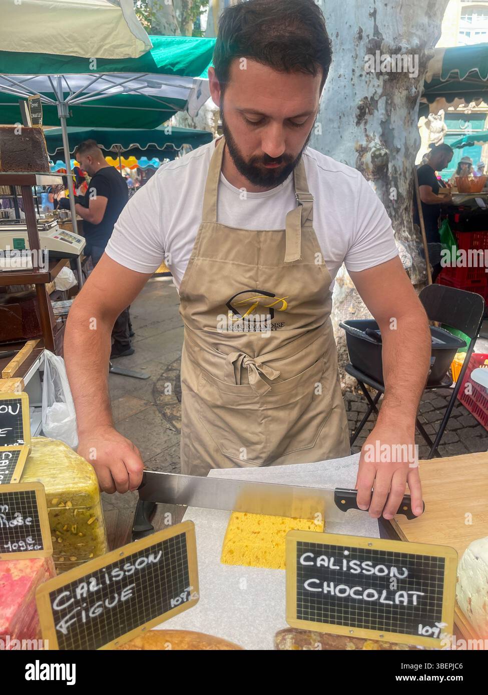 AIX-en-Provence, Francia - 10 luglio 2024: Negozio Calison al mercato pubblico in Place Richelme. Grandi pezzi di gusti diversi, di cui il venditore taglia fuori Foto Stock