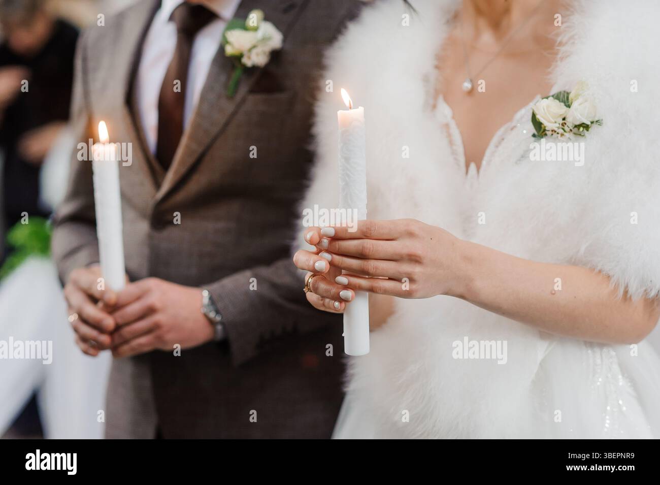 Un momento tenero durante una cerimonia nuziale raffigura una giovane sposa e uno sposo che tiene accese candele simboleggianti l'unità e l'amore eterno, vestito in modo formale Foto Stock