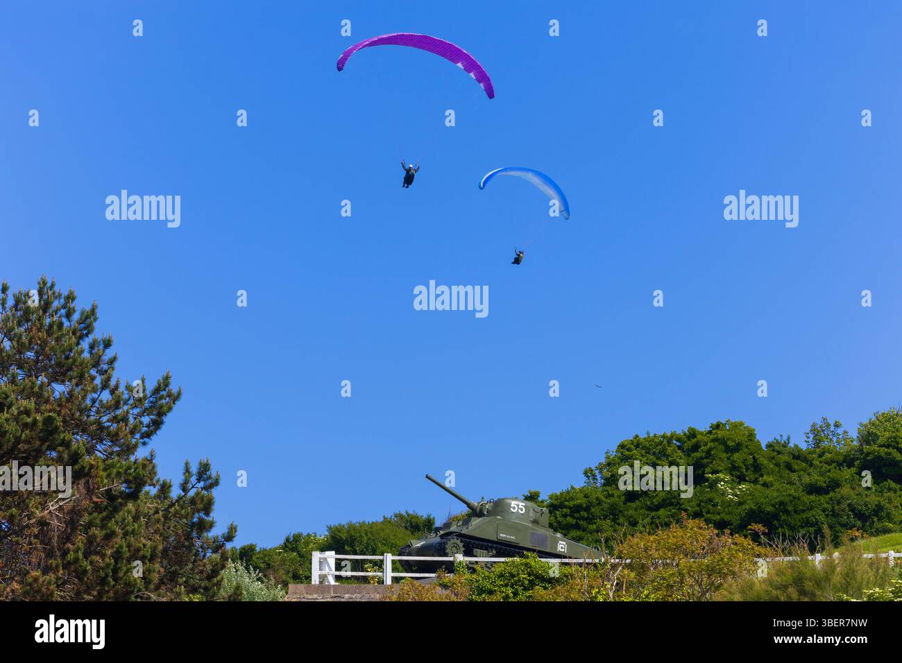 Due parapendio sorvolano il memoriale dei carri armati Sherman M4A2 ad Arromanches-les-Bains, Calvados, Normandia, Francia Foto Stock