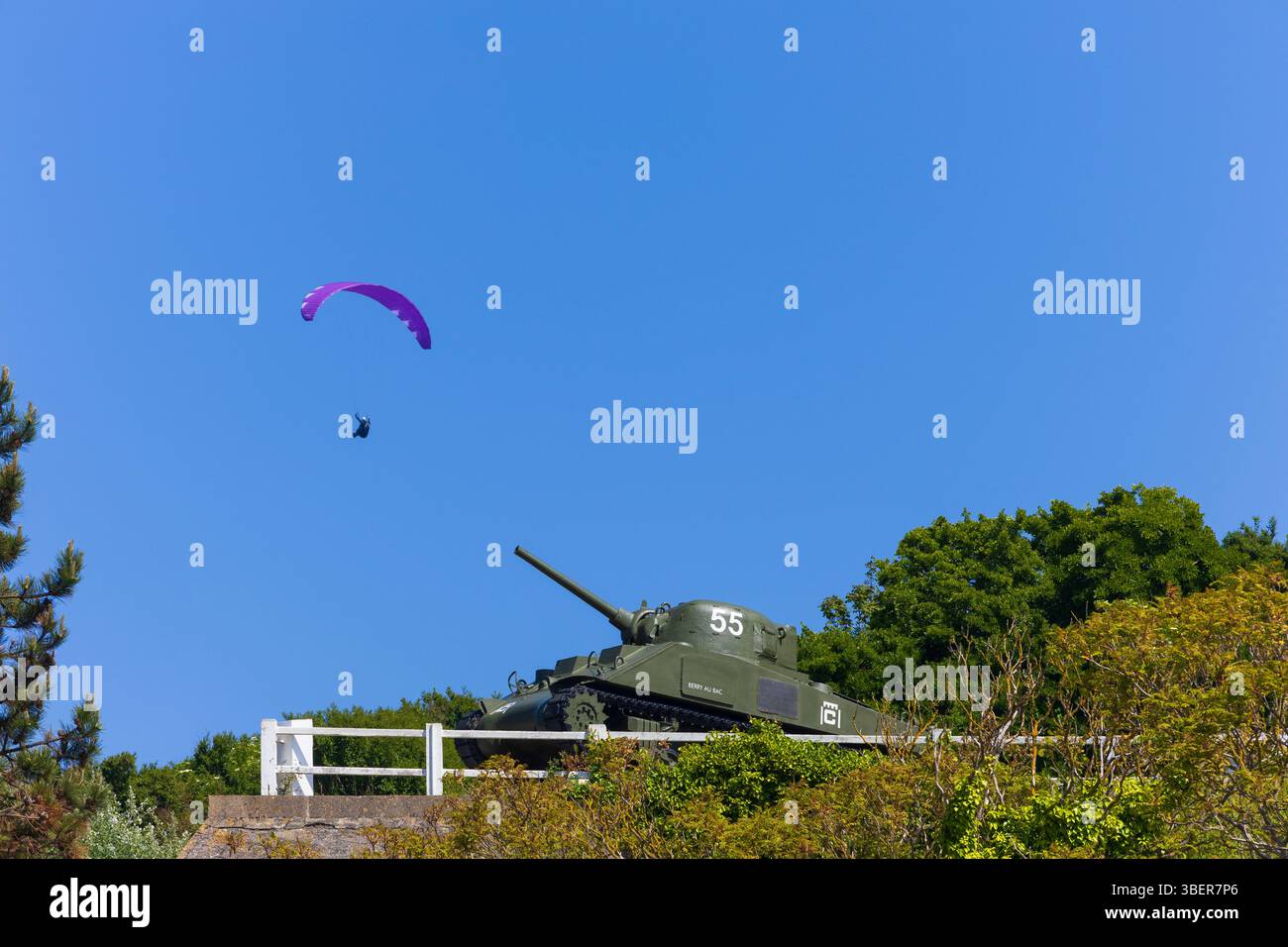 Un parapendio sorvolando il memoriale dei carri armati Sherman M4A2 ad Arromanches-les-Bains, Calvados, Normandia, Francia Foto Stock