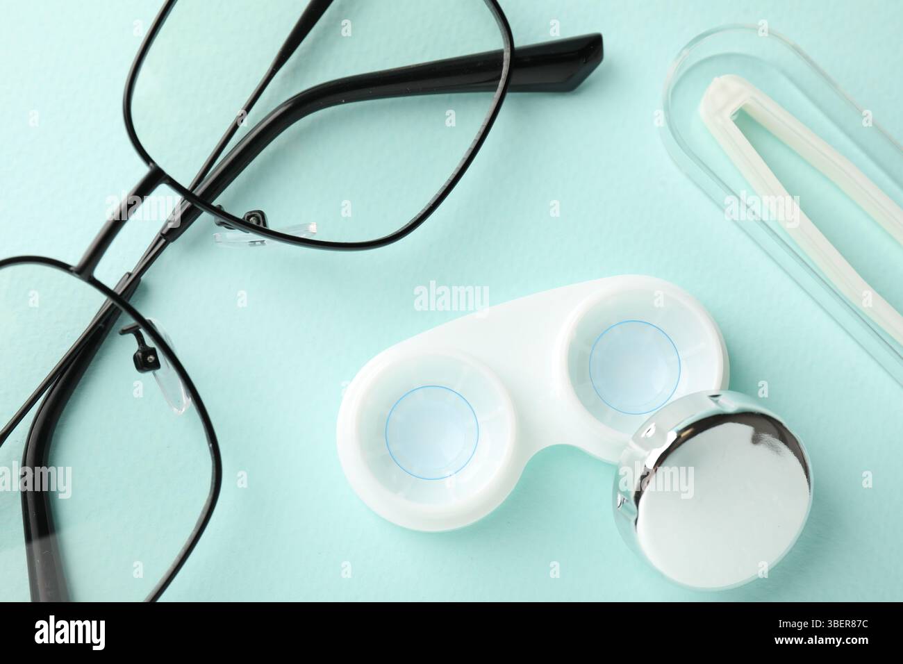 Lenti a contatto in astuccio, pinzette e occhiali su sfondo turchese chiaro, piatto Foto Stock