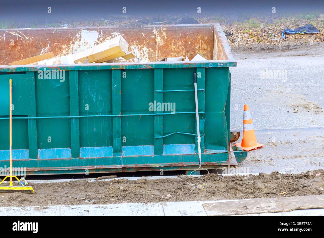I lavoratori smaltiscono i rifiuti edili in un grande contenitore situato sulla strada suburbana del cantiere Foto Stock