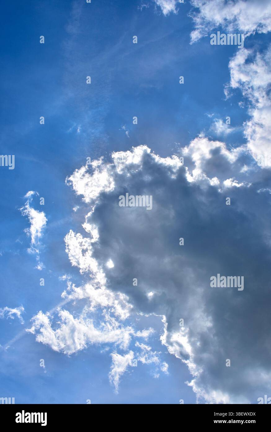 Soffici nuvole con luce solare che splende da dietro contro un cielo blu vibrante. Perfetto per temi di sfondo o natura. Foto Stock
