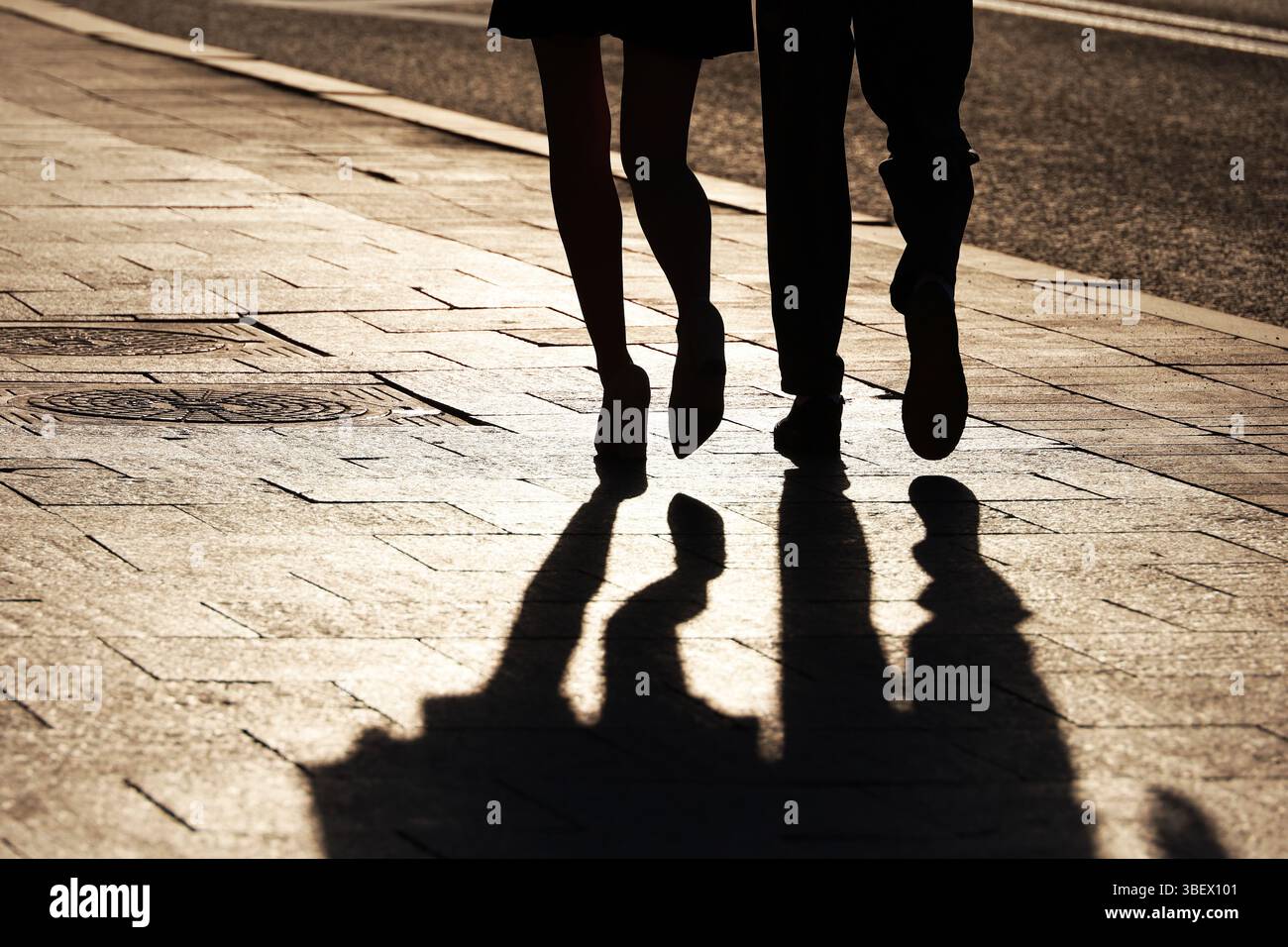 Sagome e ombre di coppia che camminano lungo la strada. Gambe femminili in scarpe con tacco alto, concetto di relazioni, vita cittadina, storie drammatiche Foto Stock