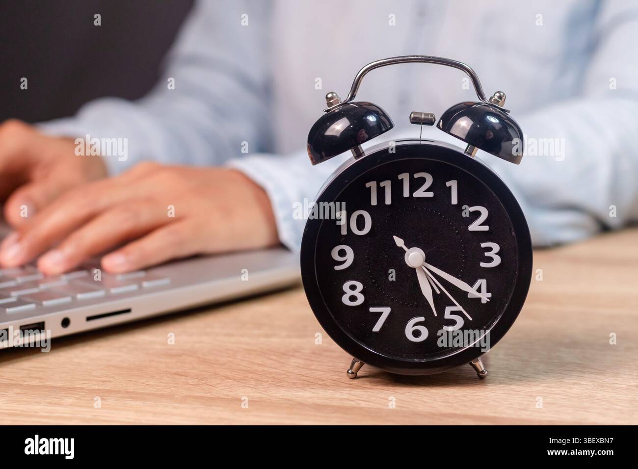 Una donna che lavora su un laptop e una sveglia nera sulla sua scrivania Foto Stock