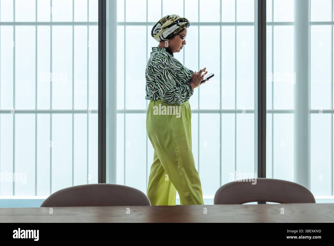Una donna indiana, proprietaria di un'azienda, utilizza con sicurezza il suo smartphone in un ambiente d'ufficio elegante e moderno. Il suo vestito vivace aggiunge un tocco dinamico, ref Foto Stock