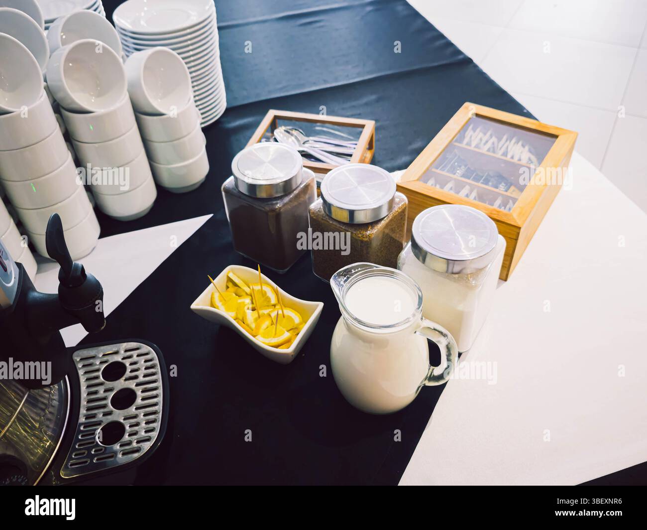 Preparazione della pausa caffè con tazze, latte, limone e vasetti da tè su una tovaglia bianca e nera - Immagine stock catturata con smartphone