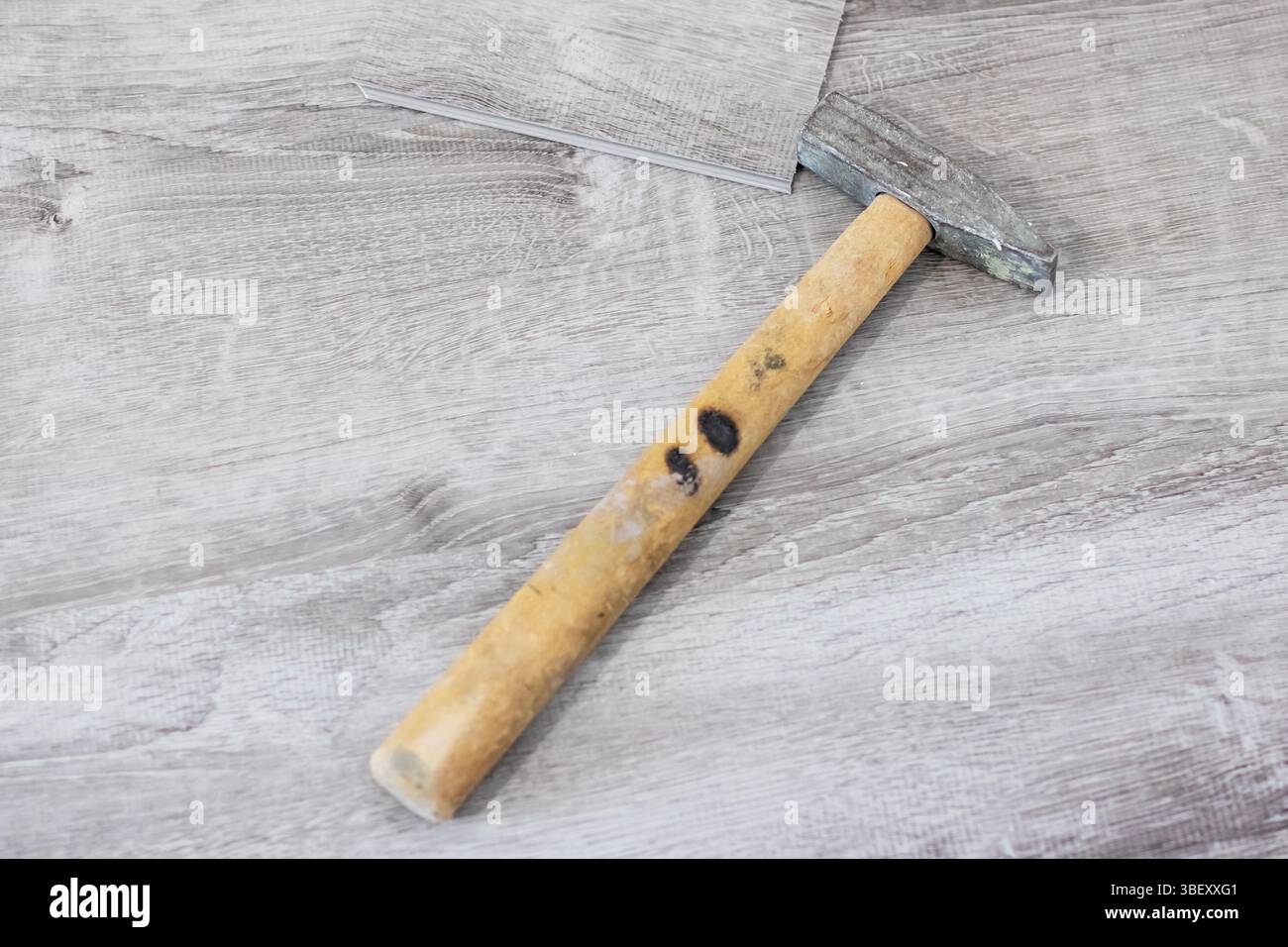 Un robusto martello dotato di un manico in legno massiccio è attualmente appoggiato su un tavolo in legno splendidamente lucidato Foto Stock