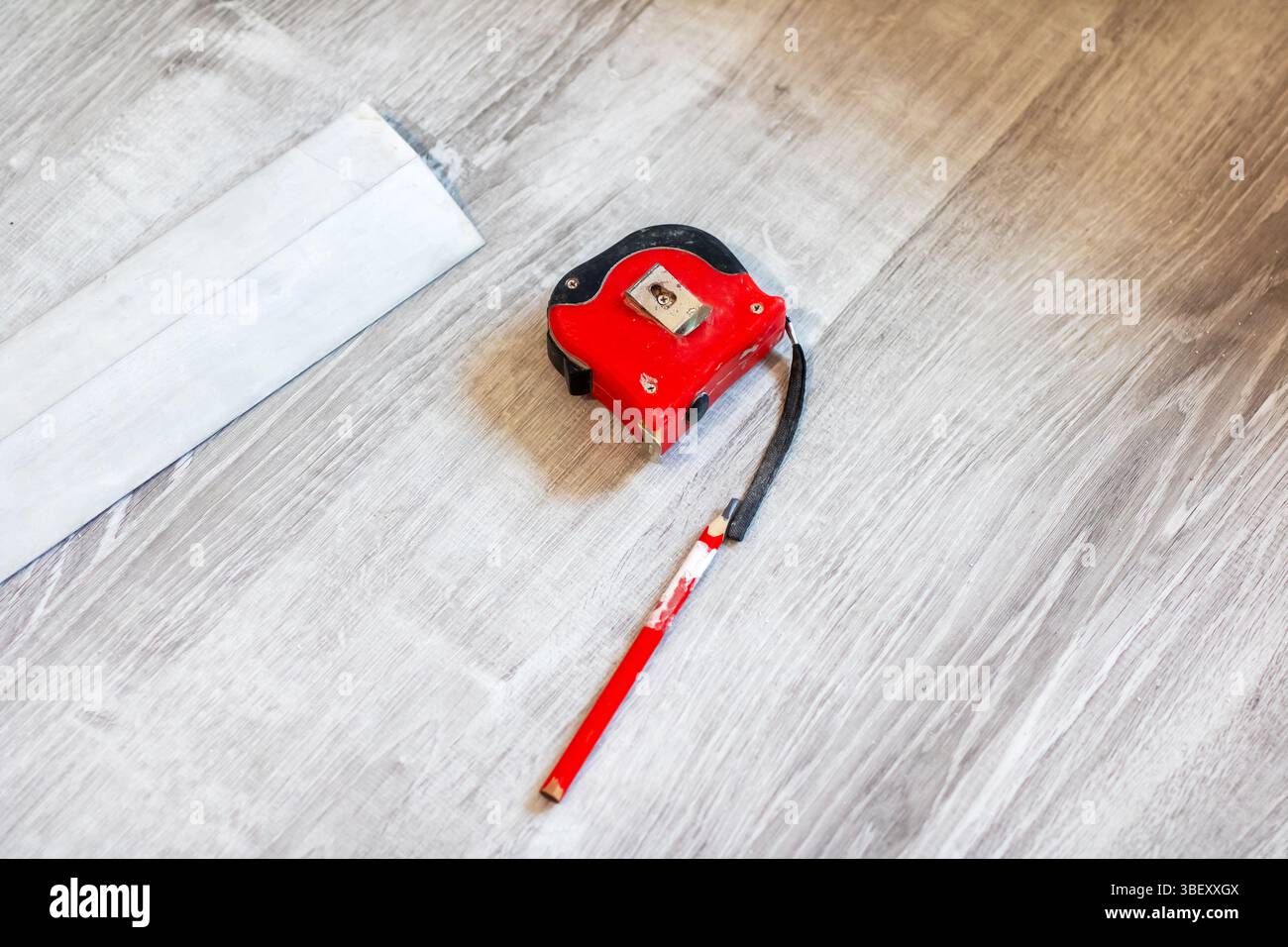 Un vivace metro a nastro rosso poggia su un pavimento di legno liscio adiacente a una matita gialla, creando un interessante contrasto visivo Foto Stock