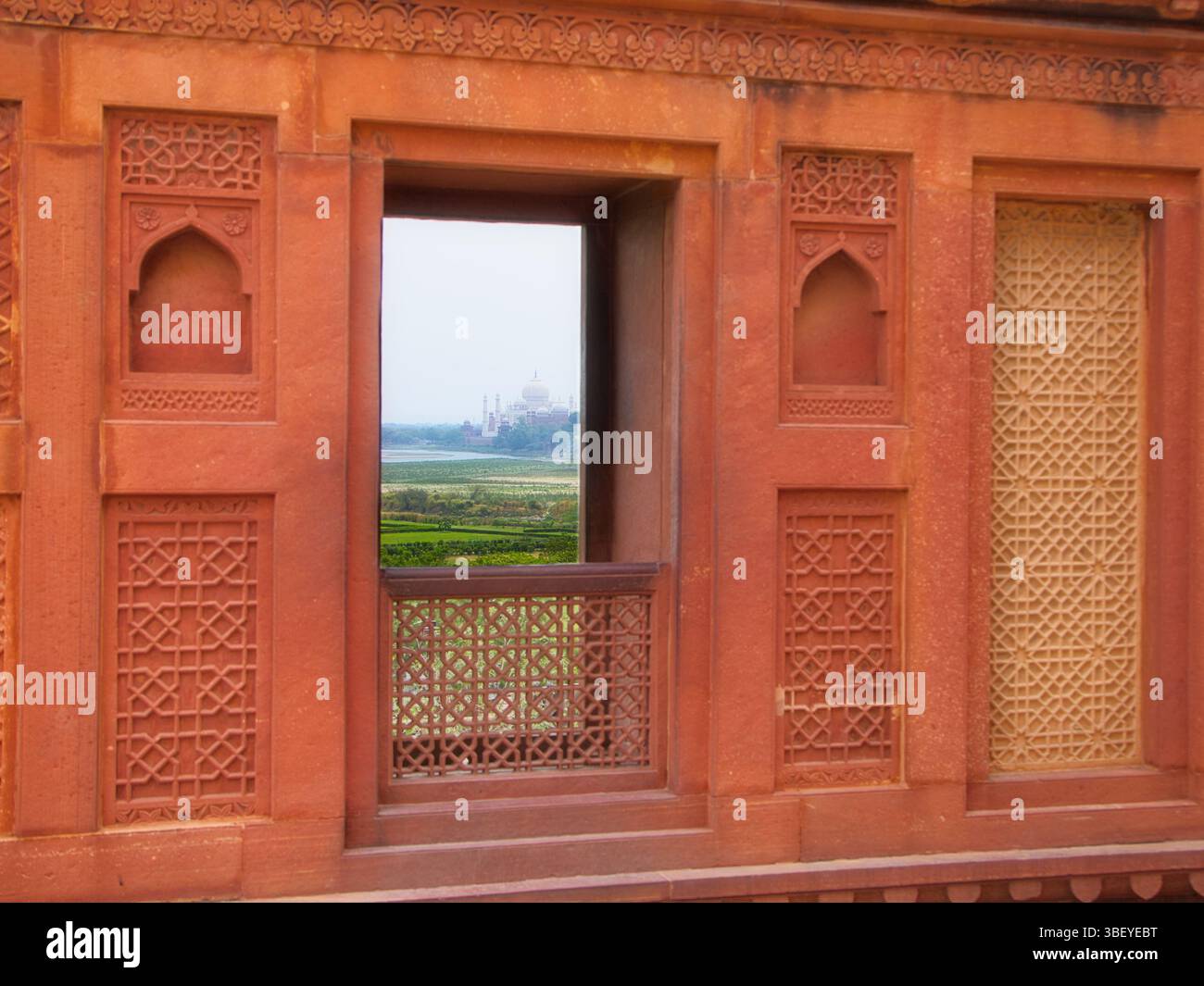 Vista panoramica del Taj Mahal attraverso una finestra di pietra arenaria rossa dell'epoca Mughal al forte di Agra, India. Foto Stock