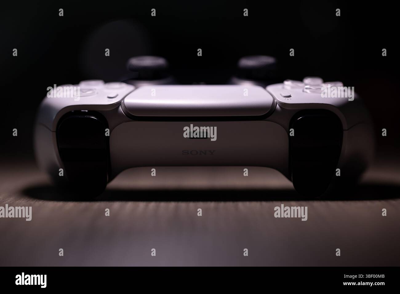 Brecht, Belgio - 18 aprile 2025: Un ritratto scuro di un controller wireless sony playstation 5 bianco originale, che si trova su un tavolo di legno sotto i riflettori. Foto Stock