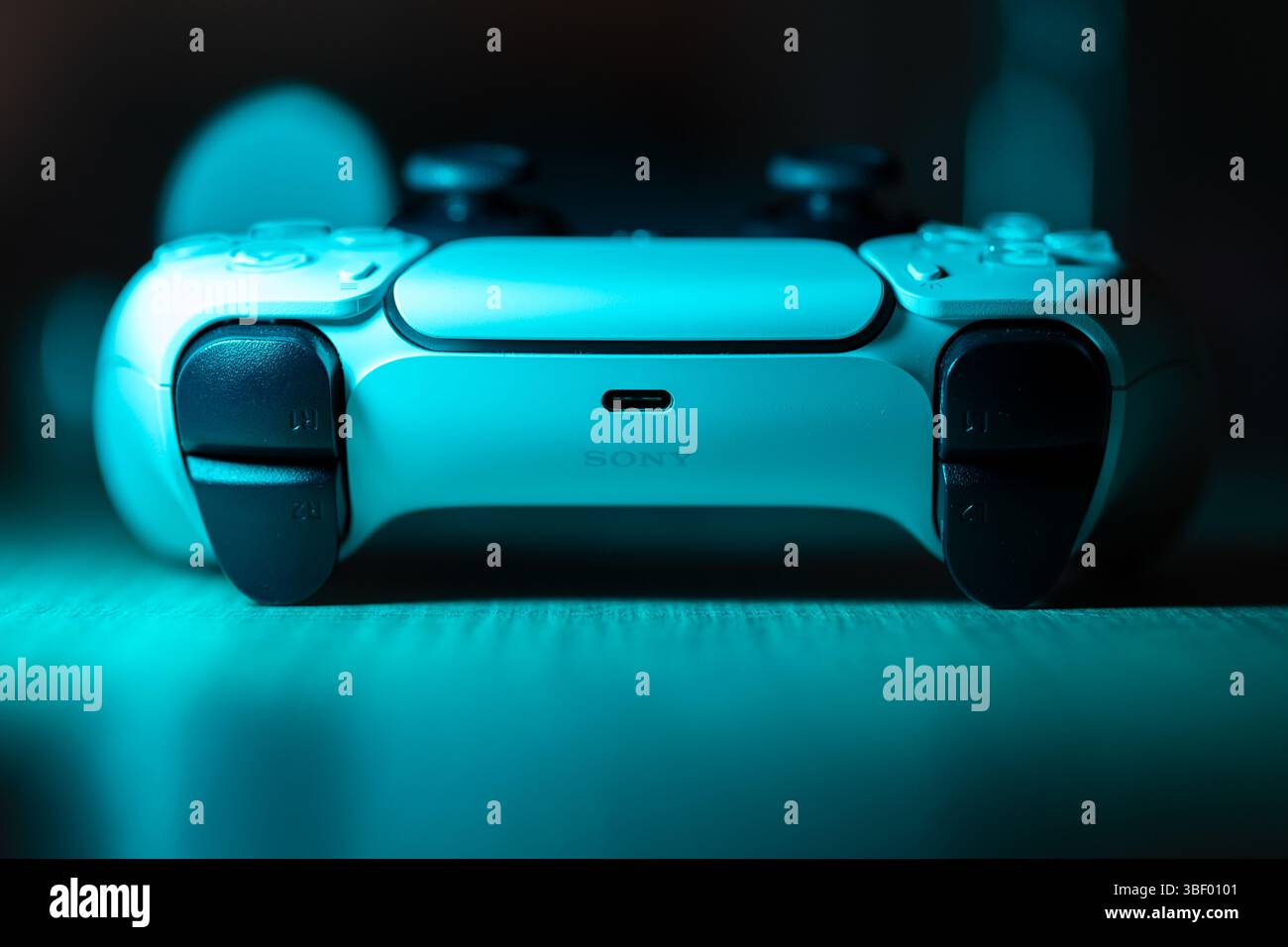 Brecht, Belgio - 18 aprile 2025: Un ritratto al neon blu di un controller wireless sony playstation 5 originale bianco appoggiato su un tavolo di legno. Pronto per PL Foto Stock