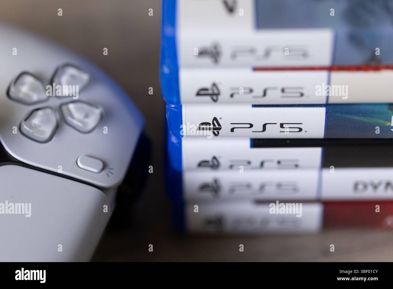 Brecht, Belgio - 18 aprile 2025: Un ritratto ravvicinato di una pila di custodie o scatole per videogiochi sony playstation 5 accanto a una PS5 wireless originale bianca c Foto Stock