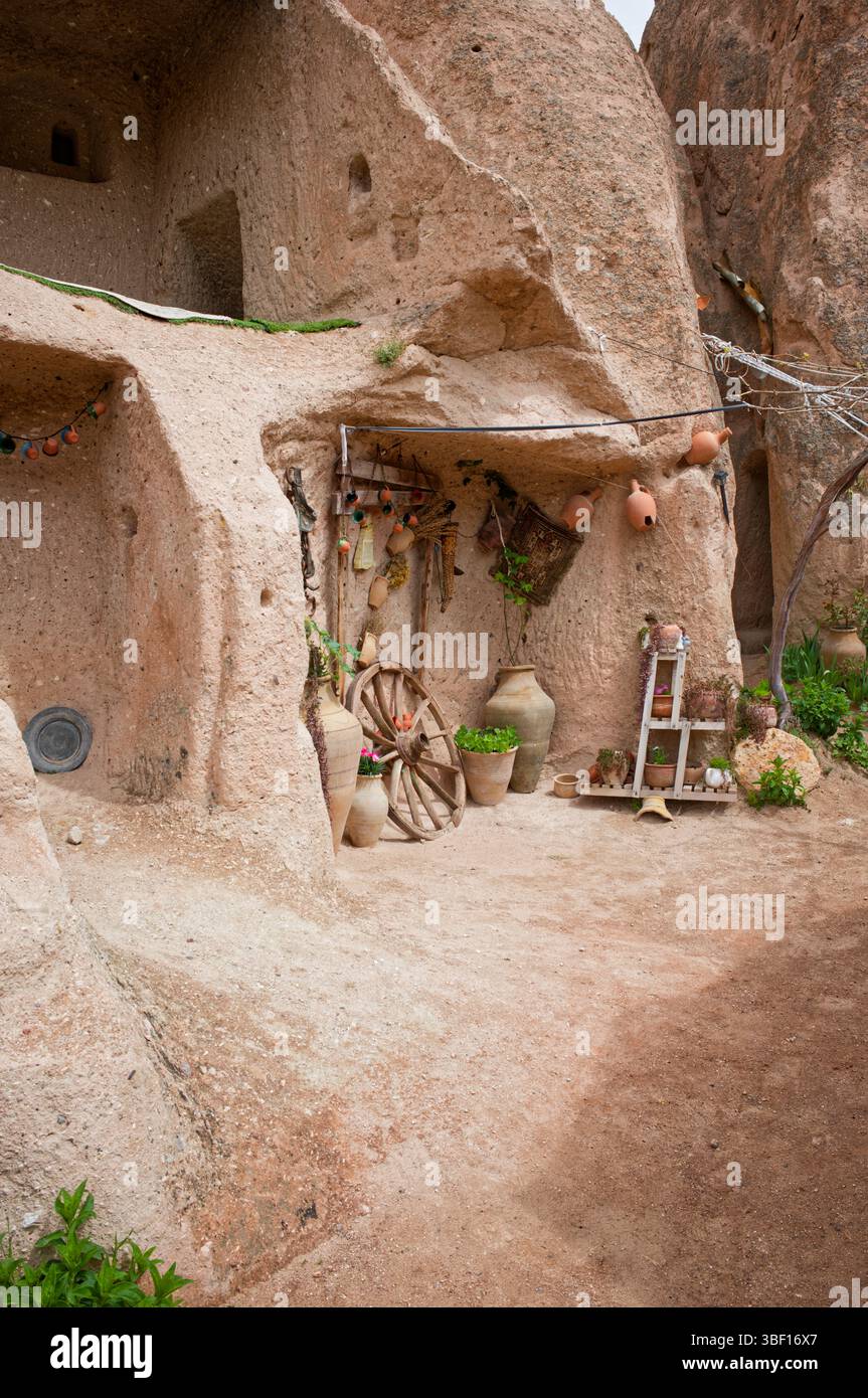 Una grotta decorata che abita in Cappadocia, Turchia. Ceramiche, piante e una ruota di legno adornano l'ingresso, riflettendo il patrimonio architettonico locale. Foto Stock