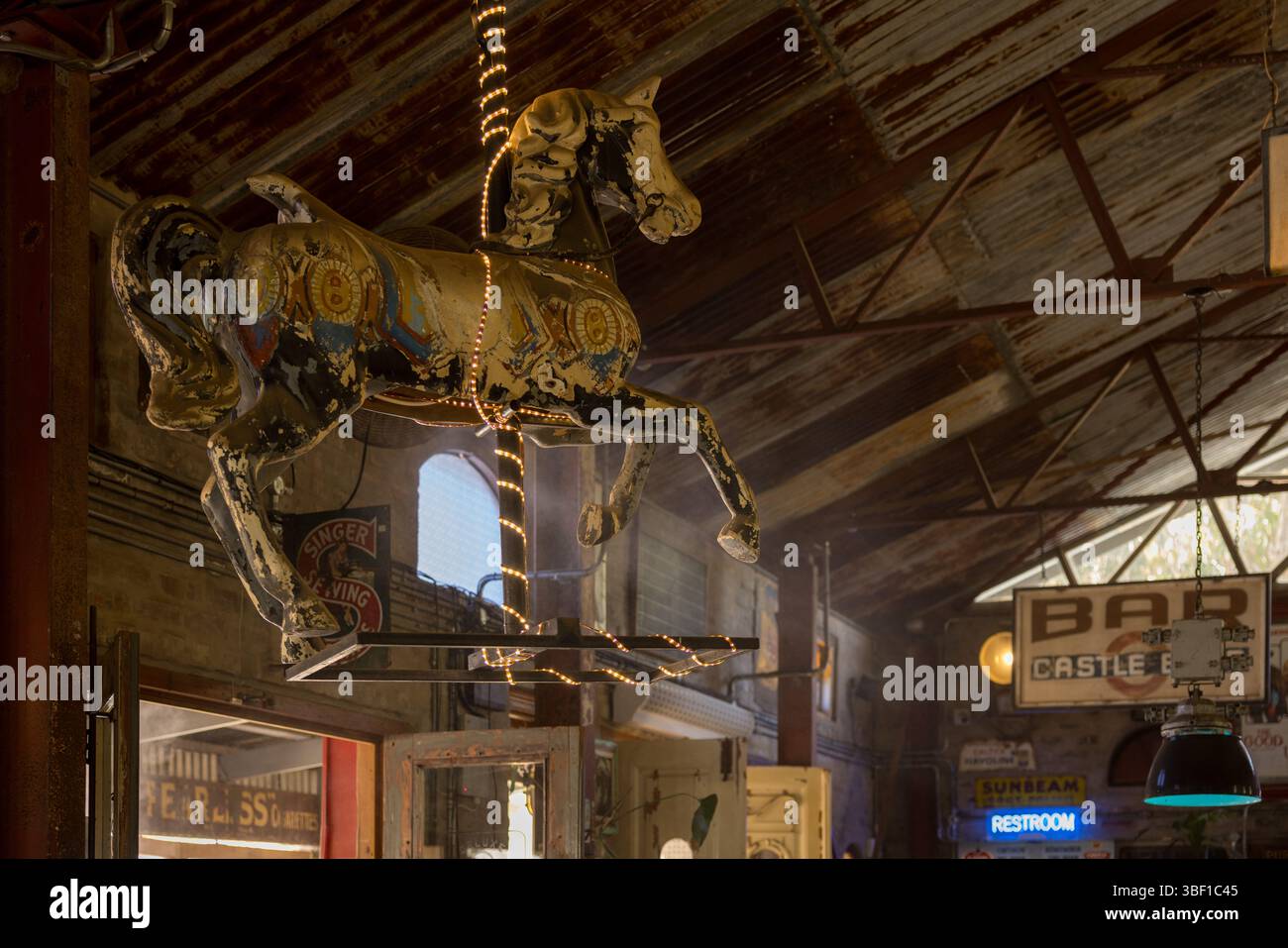 Un cavallo a giostra con luci fiabesche è appeso al soffitto di un bar sudafricano a tema vintage con segni nostalgici e tetto rustico. Foto Stock