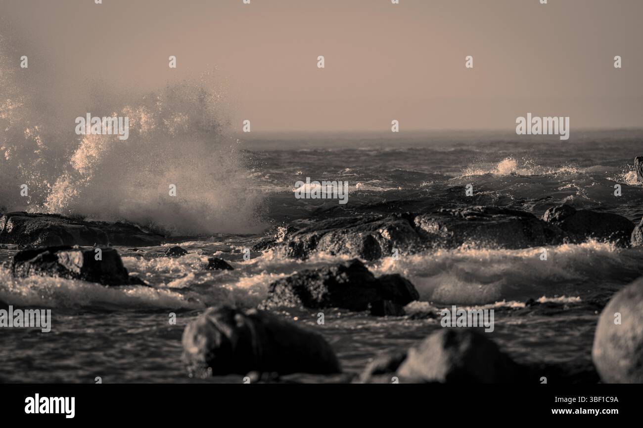 Immagine in tonalità seppia di intense onde oceaniche che colpiscono le rocce costiere in Sud Africa, mostrando un incredibile movimento di surf e acqua. Foto Stock