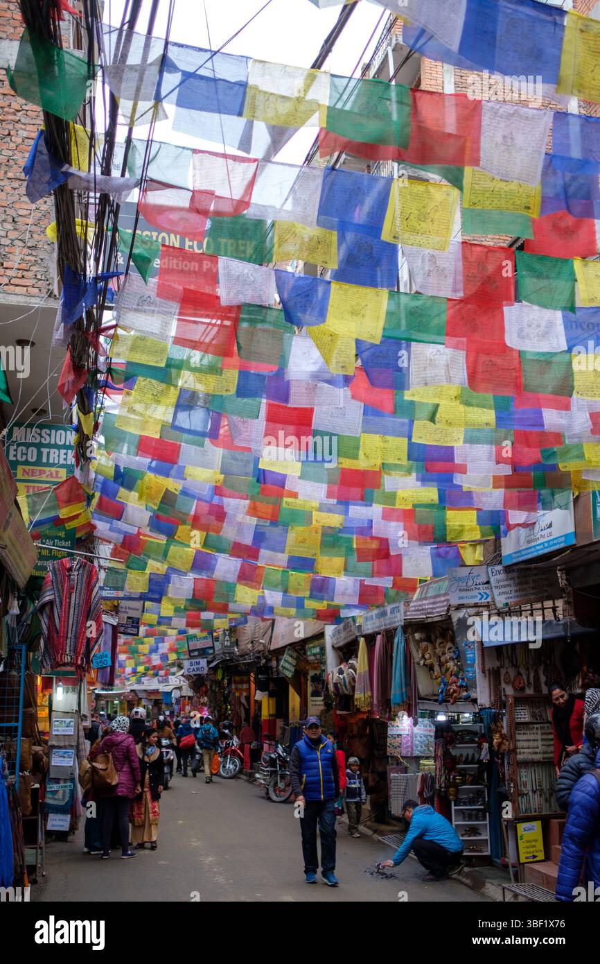 I turisti e la gente del posto fanno acquisti a Kathmandu, Nepal, sotto una tettoia di bandiere di preghiera colorate. Foto Stock