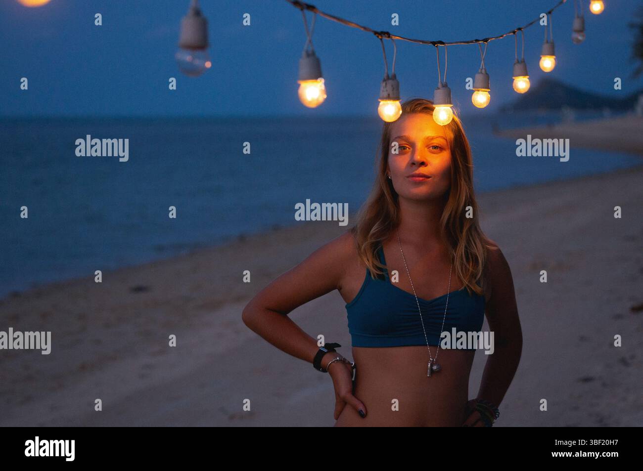 Donna sicura di sé sotto le luci a corda su una spiaggia al crepuscolo Foto Stock