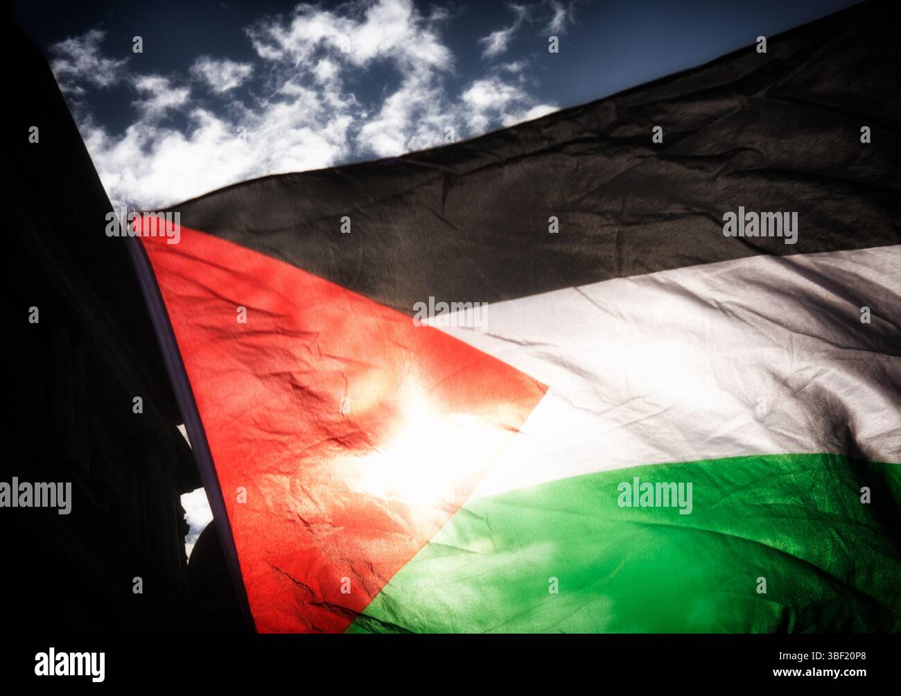 Una bandiera palestinese vola e il sole splende attraverso il suo tessuto sotto un cielo blu Foto Stock